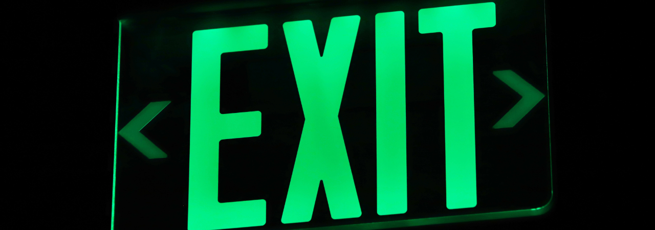 Glowing green 'exit' sign against black background