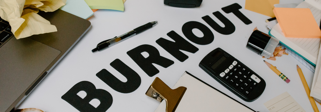 Desk with paper and stationary scattered, and word 'burnout' in black block letters as central focus