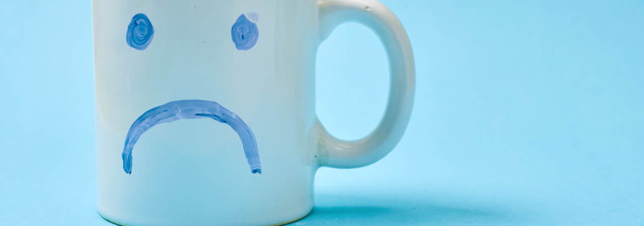 blue background with mug in foreground, featuring sad face drawn in pen