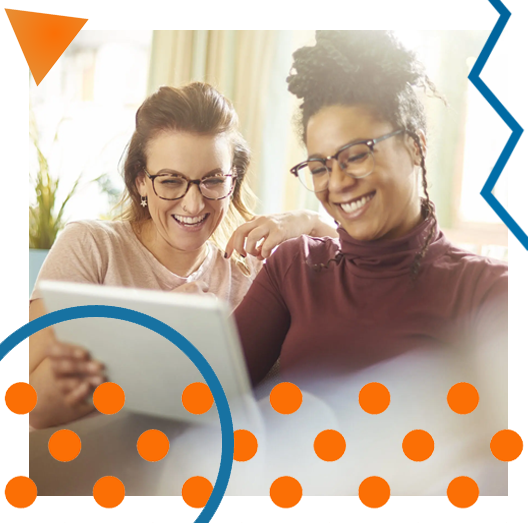 Two young women sit on a sofa and share an ipad