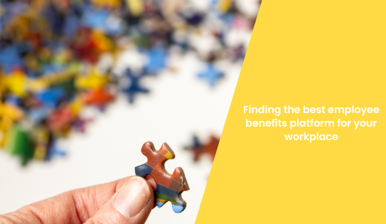 hand holding up jigsaw puzzle piece with jumbled puzzle in background. Yellow overlay shows blog title 'Finding the best employee benefits platform for your workplace'