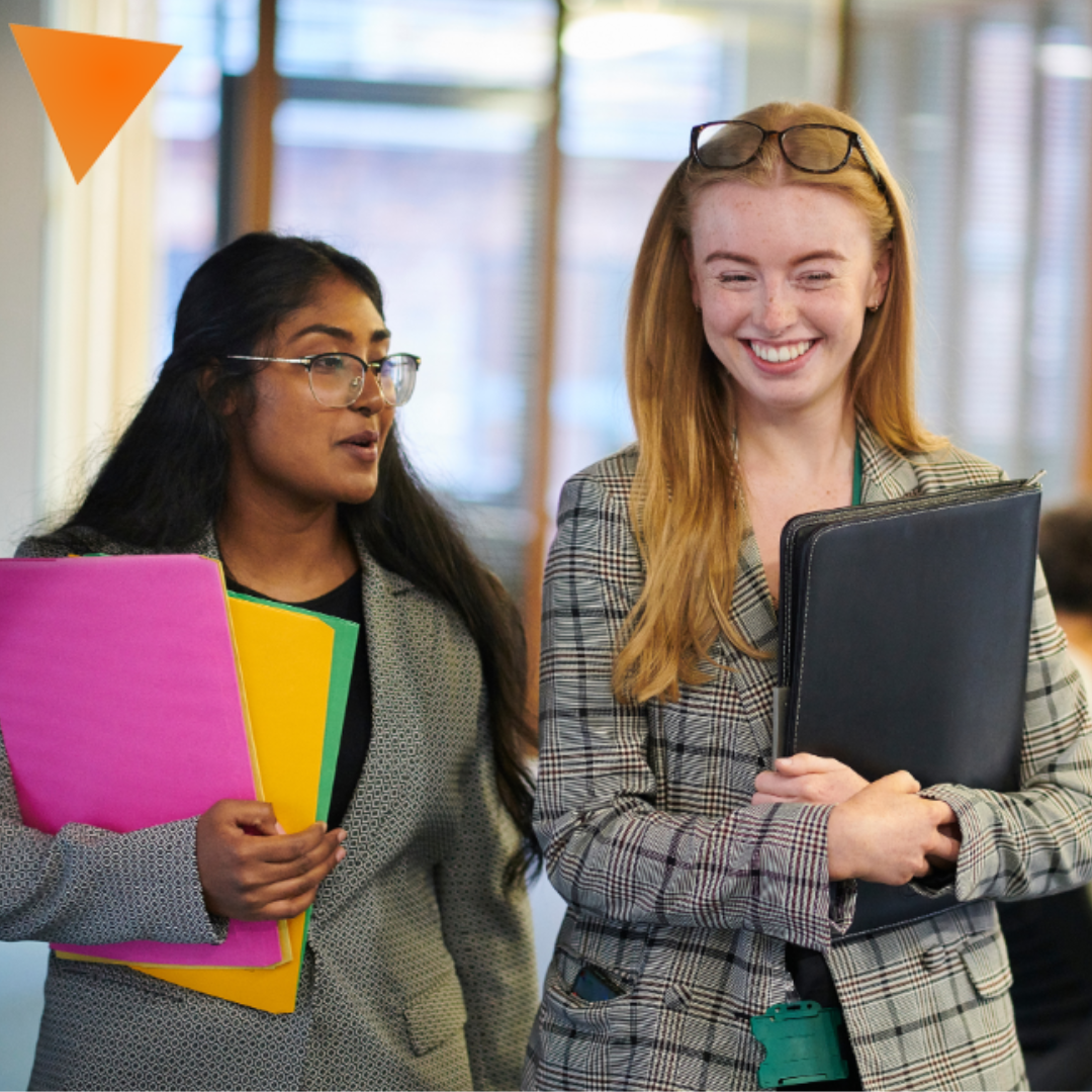 two women walking in office holding folders and smiling