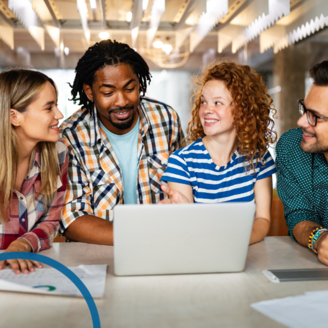 Group of four employees gathered around laptop and smiling to eachother