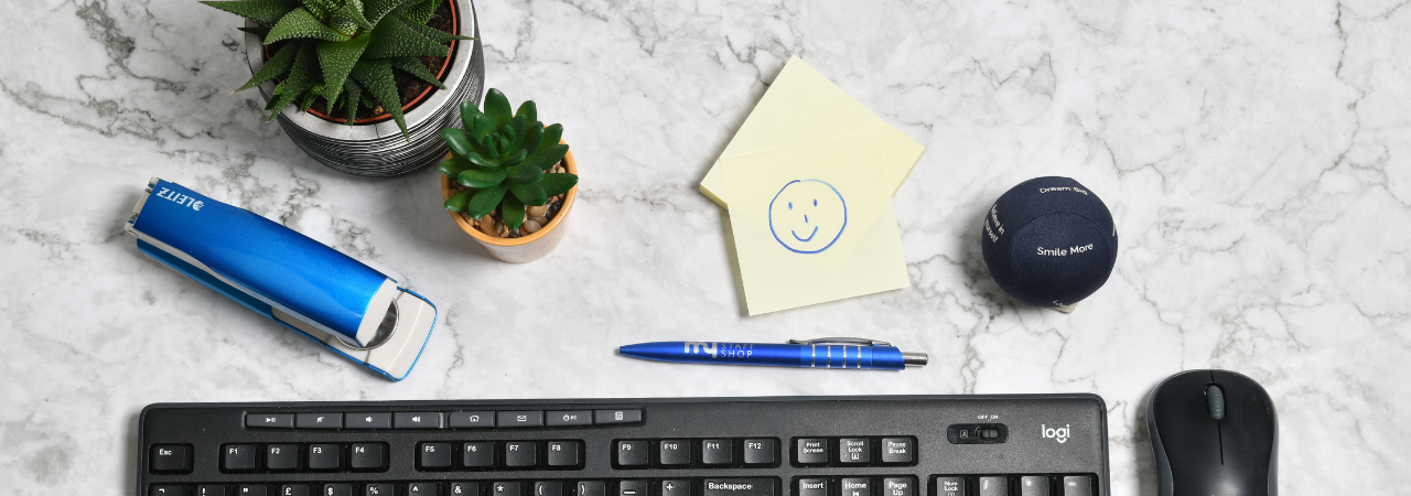 Marble background with keyboard, stationary, plants, and stress ball in focus, with smiley face drawn onto post it note