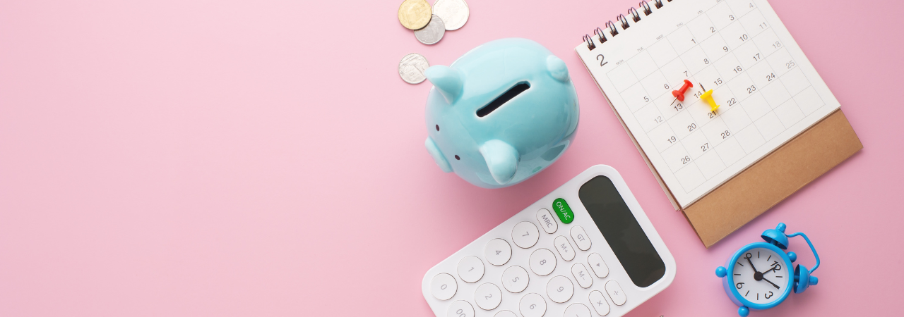 pink background flatlay of calculator, coins, calendar, and blue piggy bank